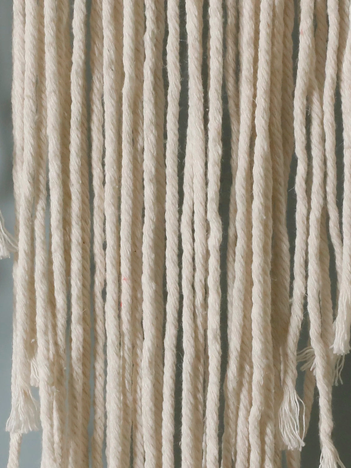 Close-up of cream-colored cotton fringe or hanging yarn strands with twisted plies and frayed ends, filling the frame against a soft gray background from My Boho Home