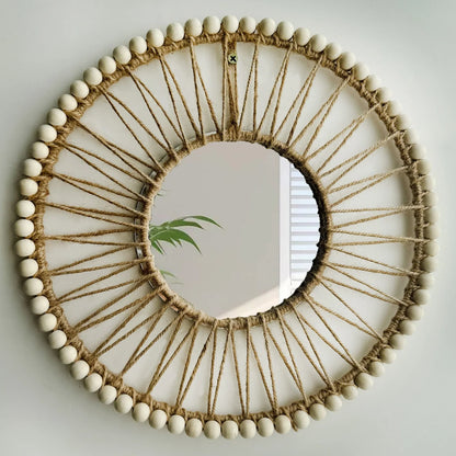 Round mirror with decorative frame made of twine and beads on a plain wall. Hand-woven Nordic round decorative mirror with Lafite grass frame and hemp rope, boho wall hanging for living room, entryway, or bedroom decor
