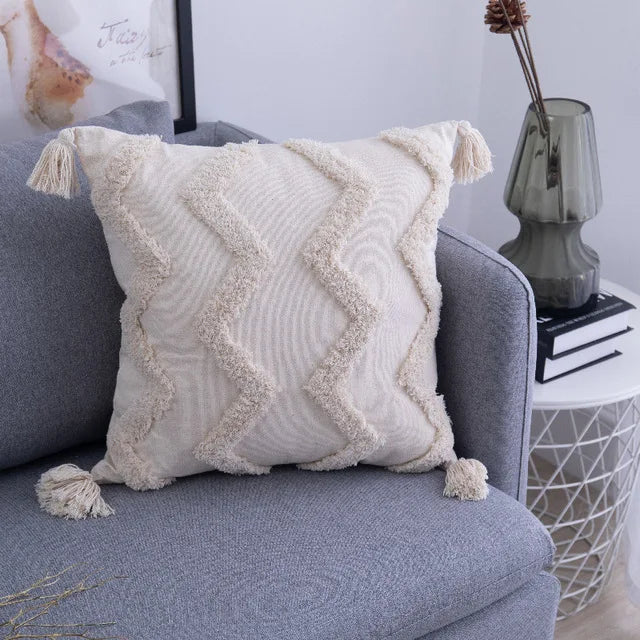 Decorative pillow with tassels on a gray sofa in a living room setting.