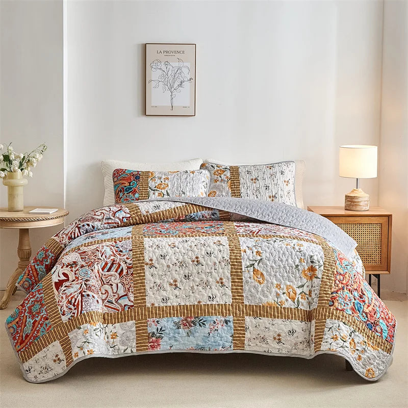 Patchwork quilt set on a bed in a bedroom with floral decor. Lightweight boho quilted bedspread set with pillow shams, soft all-season coverlet for queen, king, full, or twin beds in modern cloud pattern design.