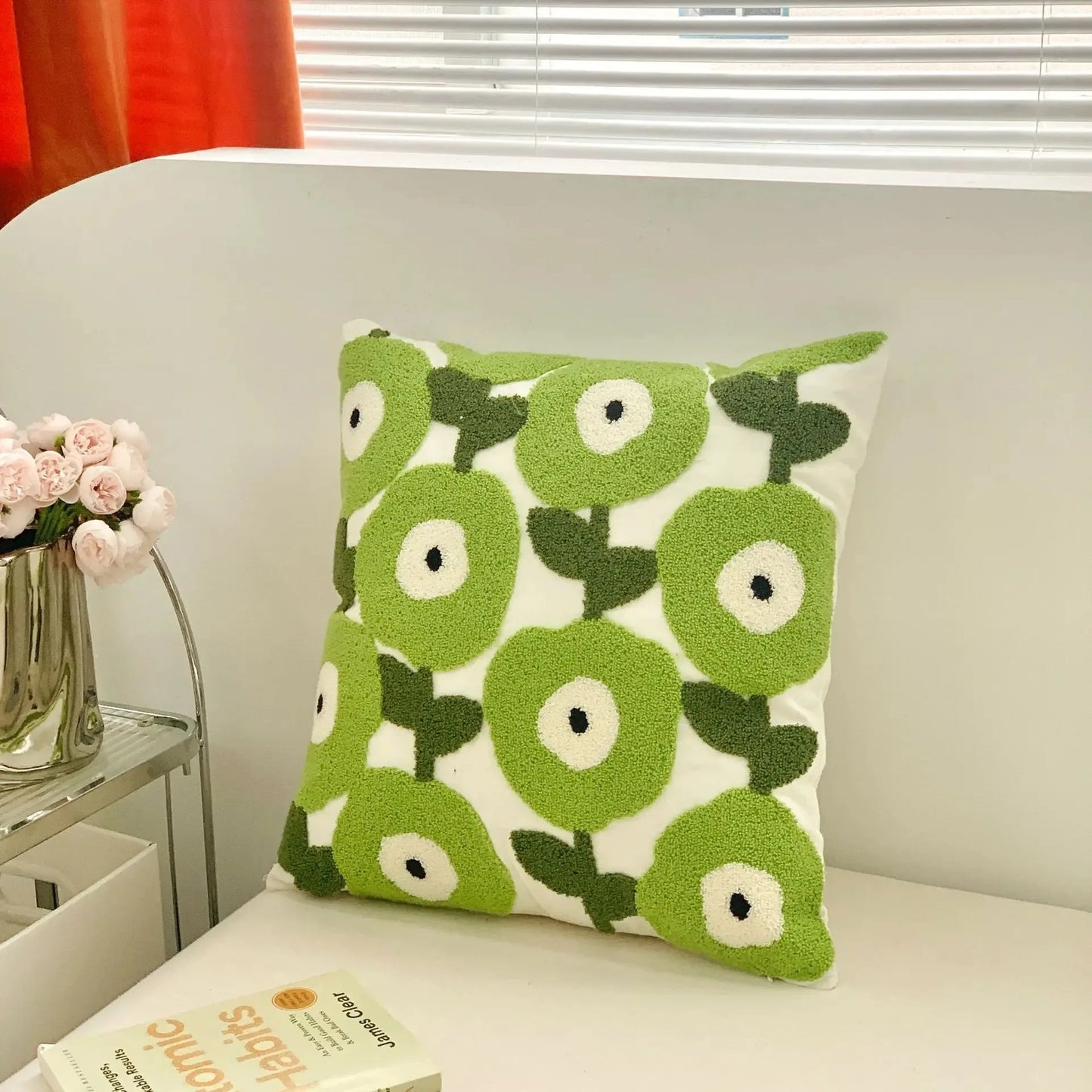 Green floral patterned pillow on a couch with a vase of flowers and book in the background.