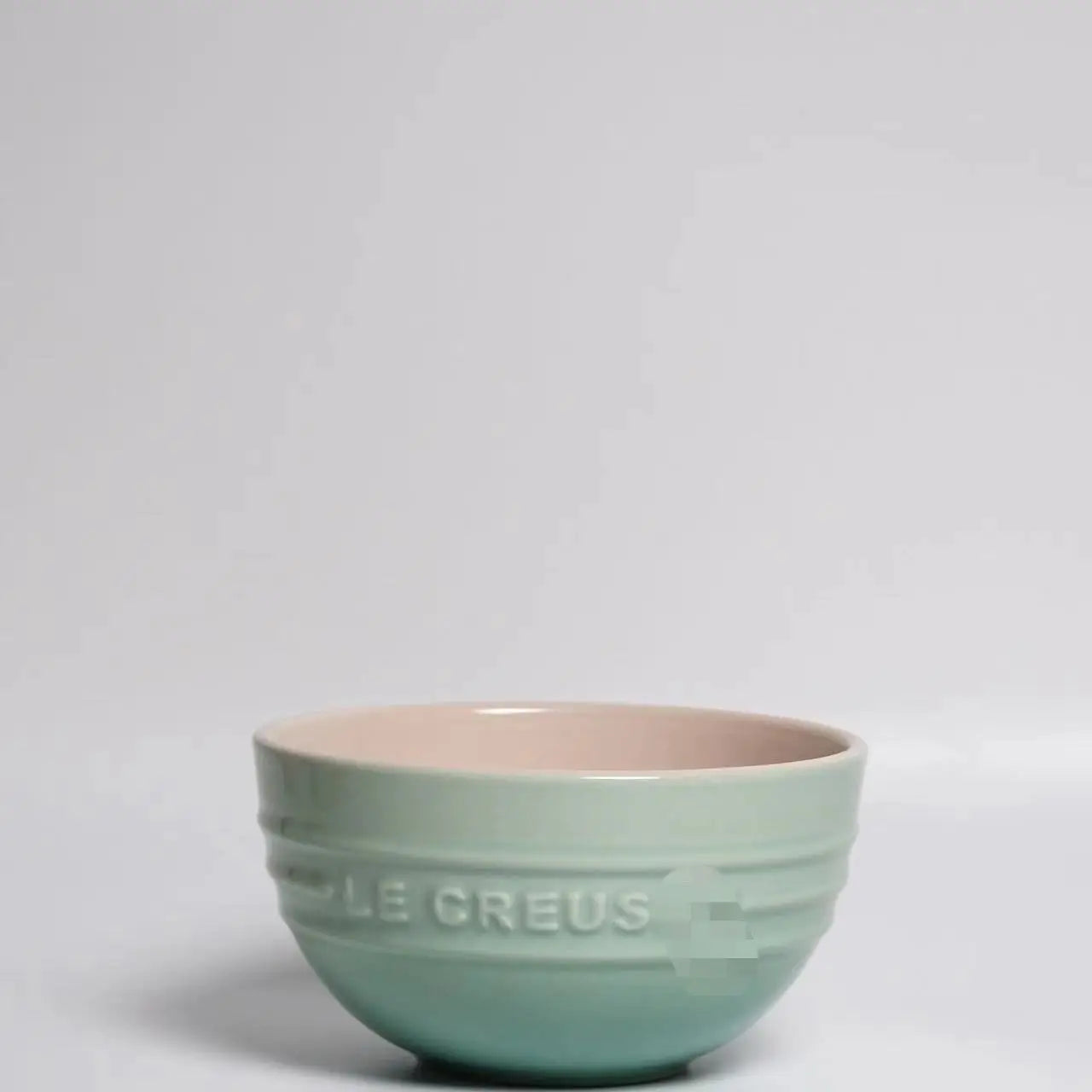 Green ceramic bowl with 'Le Creuset' branding on a light gray background Gradient ceramic rice bowl in bright colors, bone china soup and noodle bowl, dessert and pudding kitchen tableware for boho home dining