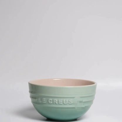 Green ceramic bowl with 'Le Creuset' branding on a light gray background Gradient ceramic rice bowl in bright colors, bone china soup and noodle bowl, dessert and pudding kitchen tableware for boho home dining