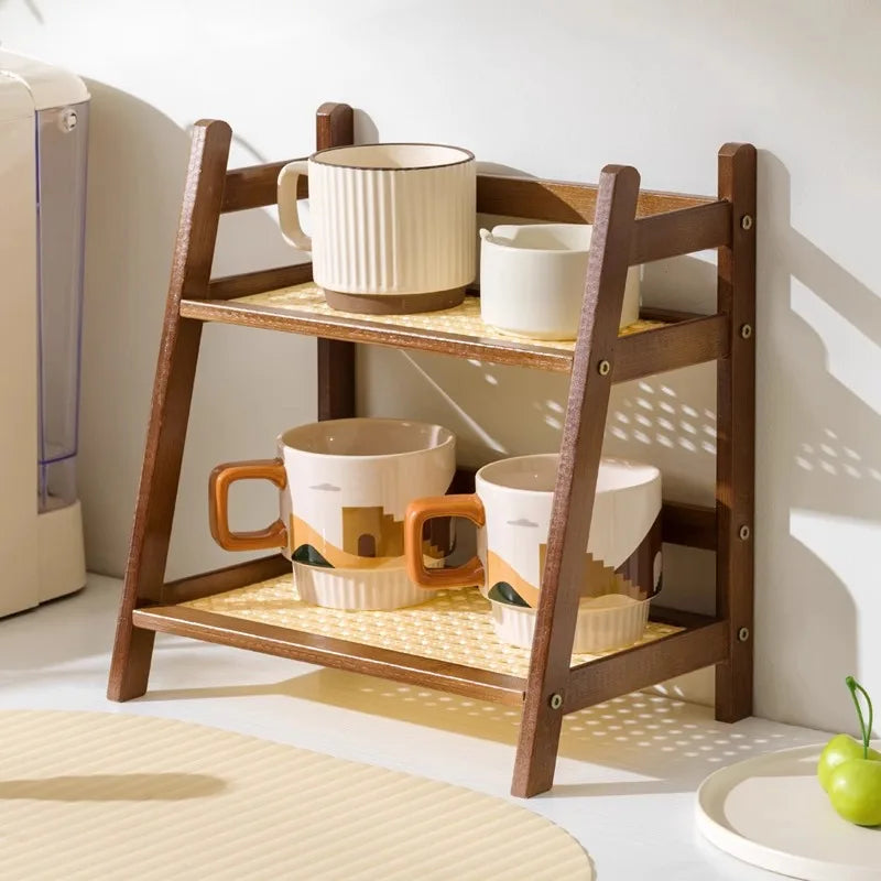 Wooden shelf with ceramic cups on a light-colored floor. 2-tier bamboo countertop organizer shelf in walnut and blonde finish, multipurpose coffee cup holder and storage rack for kitchen, bathroom, or vanity