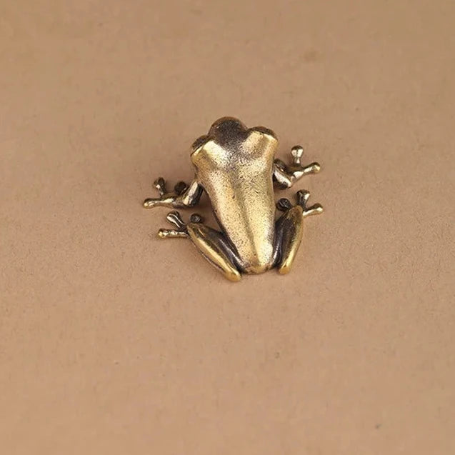Gold frog-shaped brooch on a beige background 