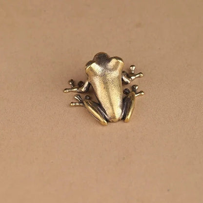 Gold frog-shaped brooch on a beige background 