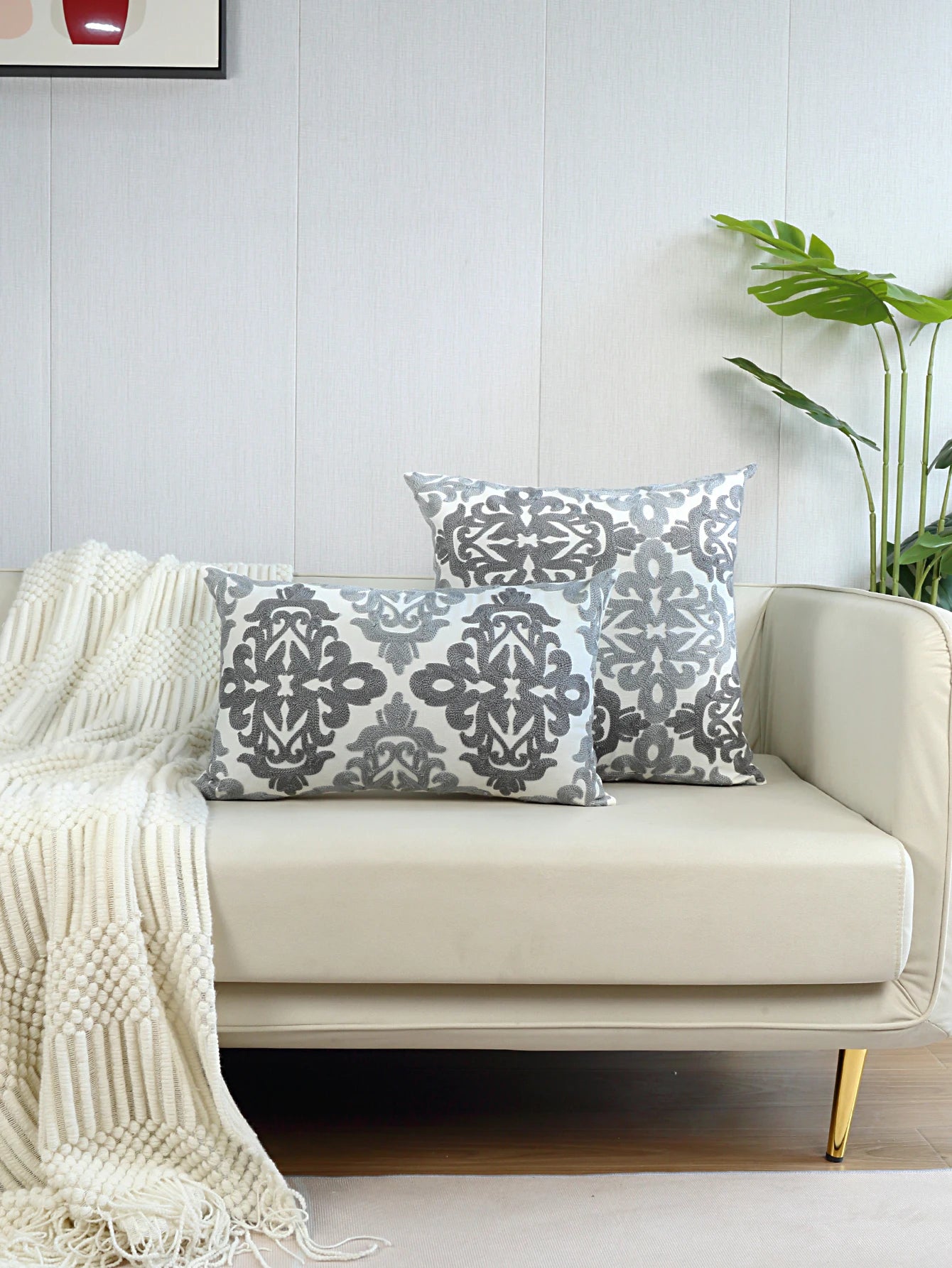 Decorative pillows on a beige sofa with a white wall and plant in the background