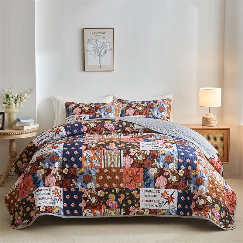 Floral patchwork comforter on a bed in a bedroom setting with a lamp and decor. Lightweight boho quilted bedspread set with pillow shams, soft all-season coverlet for queen, king, full, or twin beds in modern cloud pattern design.