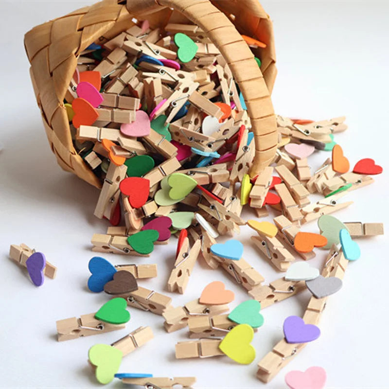 Colorful wooden clothespins with heart-shaped decorations spilling out of a wicker basket on a white background.