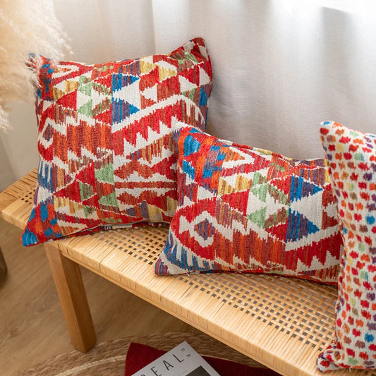 Colorful patterned pillows on a wooden bench with a neutral background. Bohemian Aztec woven pillow cover, geometric jacquard cushion for sofa, bed, or living room decor in neutral cotton blend fabric.