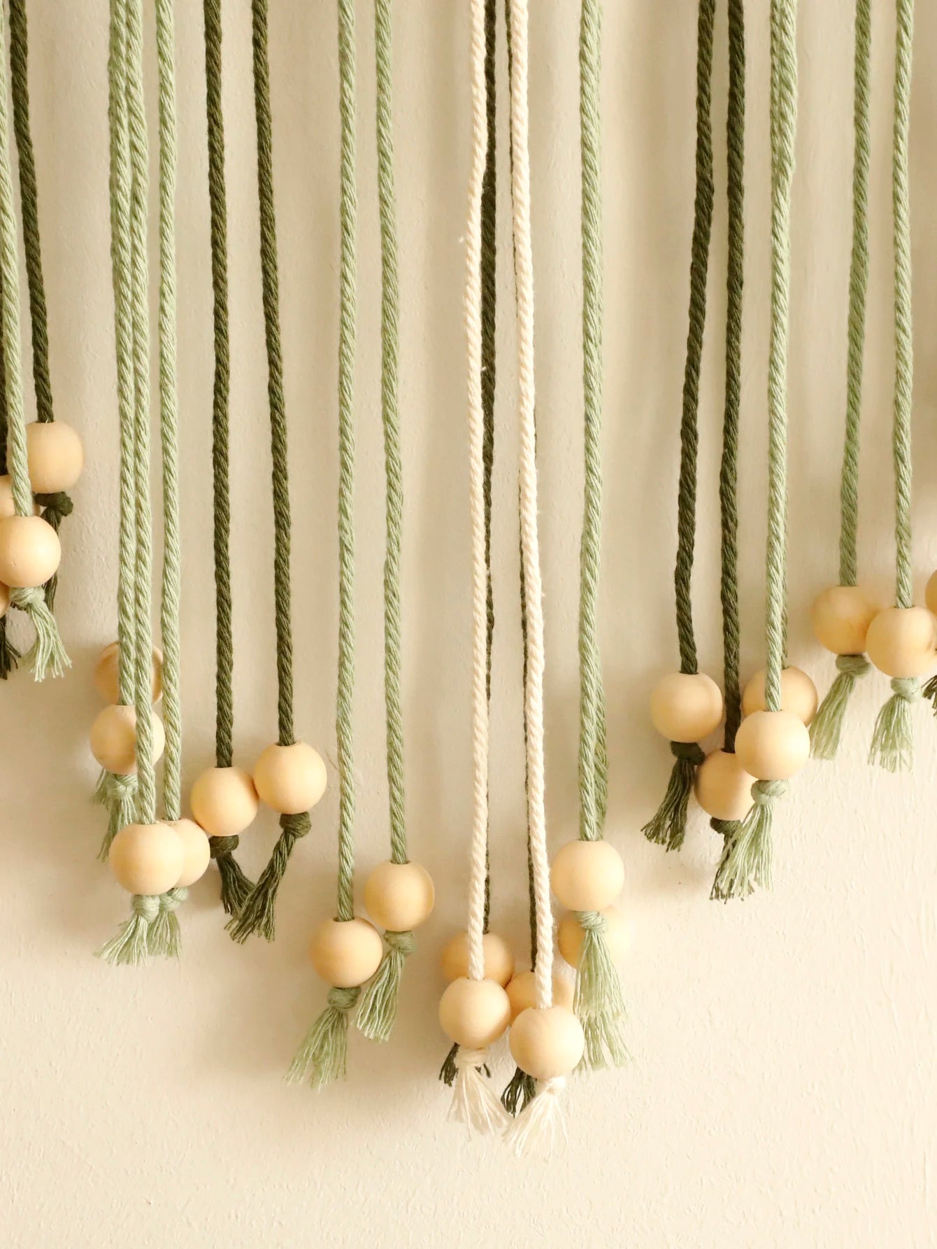 Decorative hanging with ropes and wooden beads on a plain background