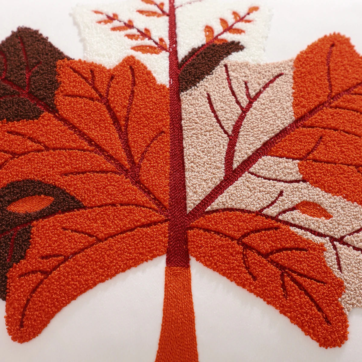 Close-up of a textured leaf design on a white background. Velvet pillow cover with embroidered pumpkins, sunflowers, and autumn leaves – cozy fall home décor for sofa or living room.
