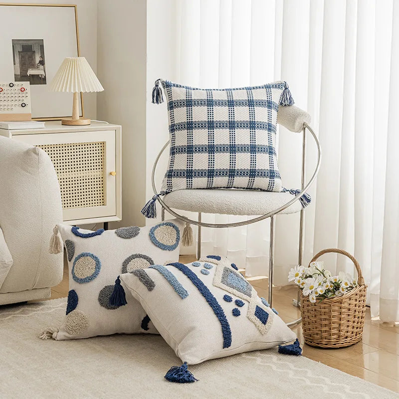 Decorative pillows with geometric patterns on a chair in a room setting. Nordic blue tufted cushion cover with geometric stripe and grid crochet pattern, tassel pillow cover for sofa, bed, and boho home decor