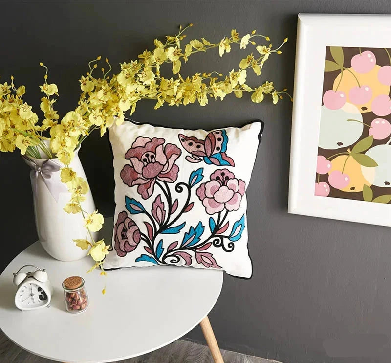 Decorative pillow with floral design on a table against a gray wall with a framed picture. floral embroidery on linen cotton cushion cover – boho home decor accent