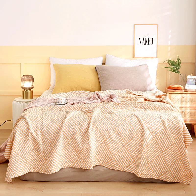 Bed with pink quilt and pillows in a bedroom setting. Boho Lightweight microfiber summer blanket for bed or sofa, cooling breathable throw for home, dorm, or office naps with geometric jacquard pattern.