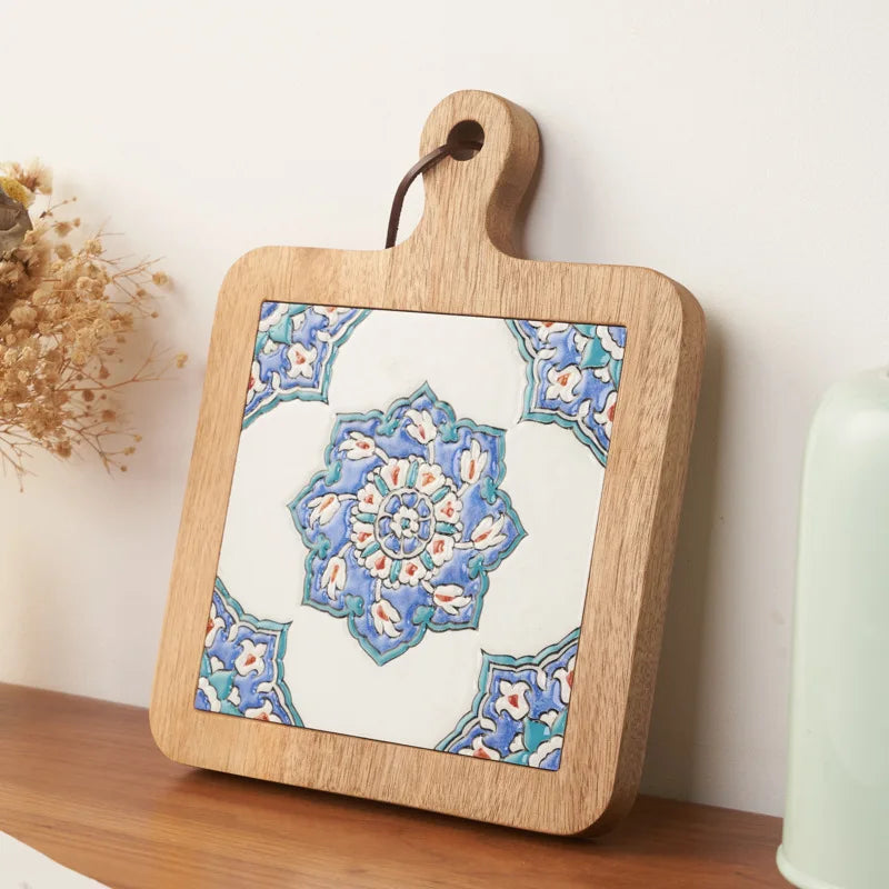 Wooden cutting board with a decorative tile design on a wooden surface.
