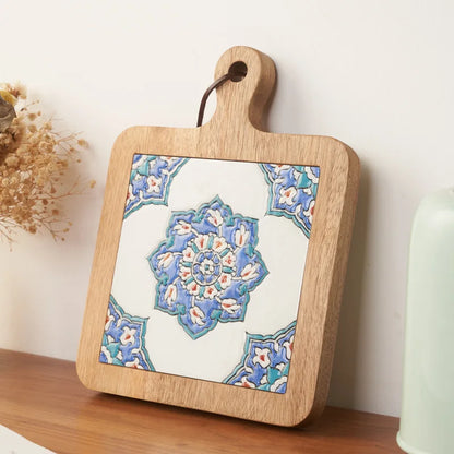 Wooden cutting board with a decorative tile design on a wooden surface.