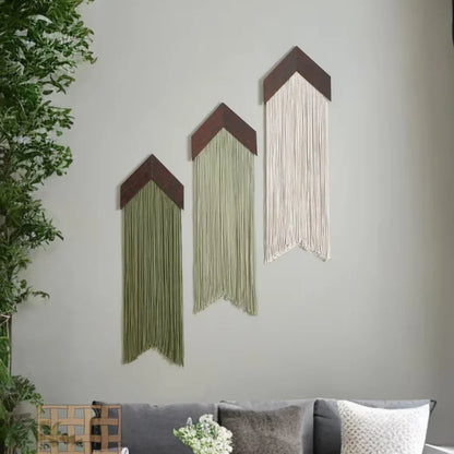 Three wall art pieces with string designs on a gray wall, with plants and a sofa in the background.