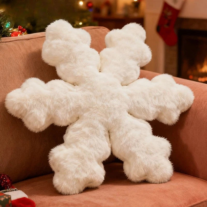 A fluffy white snowflake-shaped throw pillow resting on a dusty rose sofa in a cozy, warmly lit living room setting.