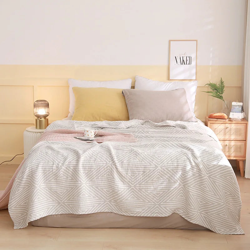 Bedroom with a bed featuring a white textured comforter, yellow and gray pillows, and a nightstand with a lamp. Boho Lightweight microfiber summer blanket for bed or sofa, cooling breathable throw for home, dorm, or office naps with geometric jacquard pattern.