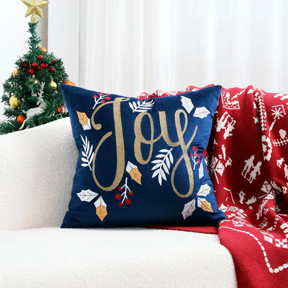 Decorative pillow with 'Joy' text on a couch with a Christmas tree in the background