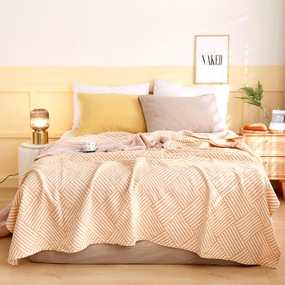 Bed with a patterned pink and white blanket, yellow and gray pillows, and a 'Naked' framed picture on a yellow wall. Boho Lightweight microfiber summer blanket for bed or sofa, cooling breathable throw for home, dorm, or office naps with geometric jacquard pattern.