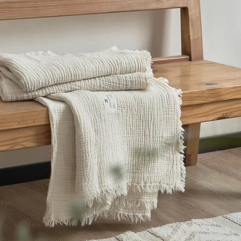 Folded textured blanket on a wooden surface Maillard cotton gauze blanket with tassels, four-layer muslin throw for sofa, bed, and boho home decor