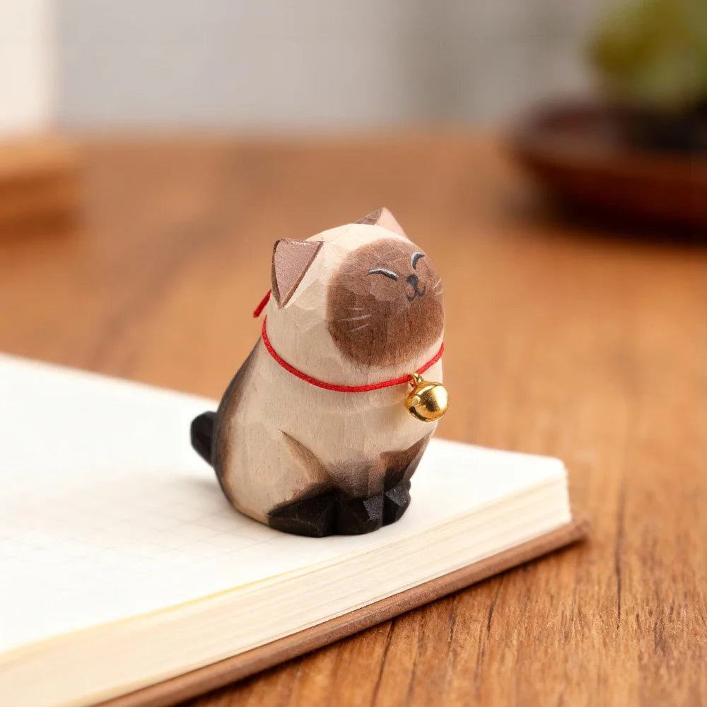 Cat-shaped wooden figure with a red string and gold bell on a wooden surface.