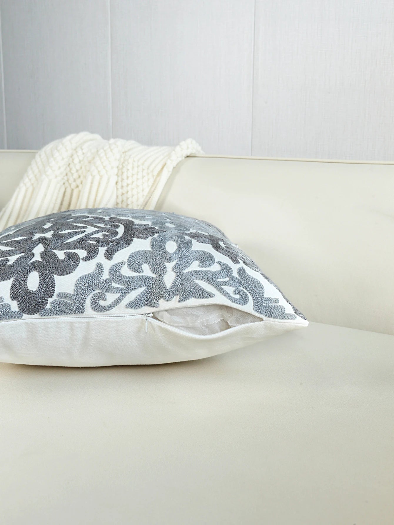 Gray floral-patterned pillow on a beige sofa with a white blanket.
