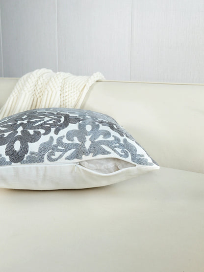 Gray floral-patterned pillow on a beige sofa with a white blanket.