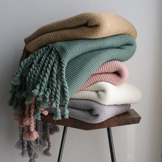 Stack of colorful knitted blankets on a wooden stool against a neutral background
