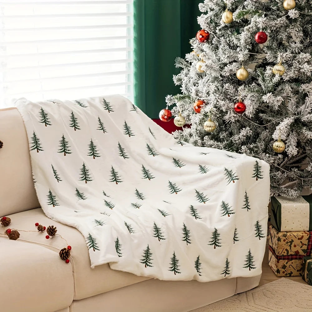 White blanket with green tree pattern draped over a beige couch next to a decorated Christmas tree.