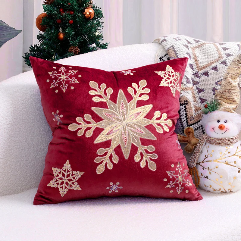 Red pillow with gold snowflake design on a couch with Christmas decorations. Embroidered Merry Christmas pillow cover with snowflake design – festive red and white holiday cushion for sofa or bedroom décor.