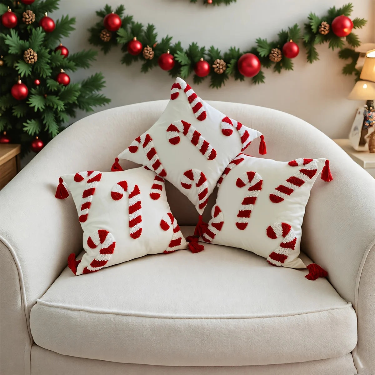 Decorative pillows with candy cane pattern on a white armchair, Christmas tree and garland in the background.