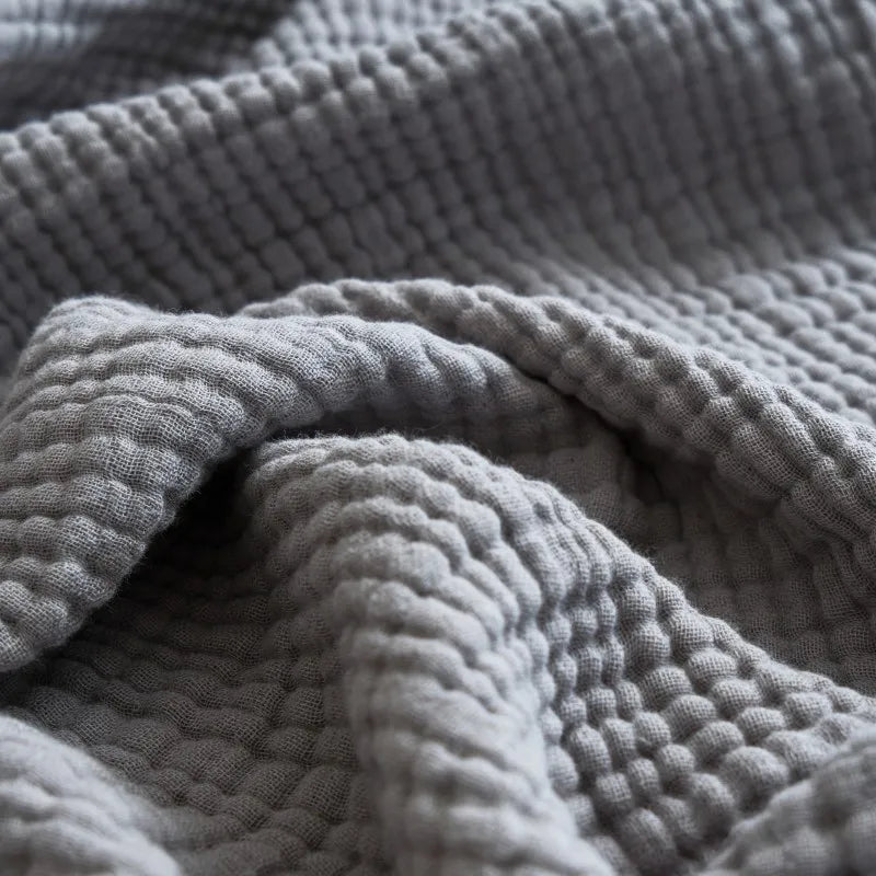 Close-up of a textured gray blanket Maillard cotton gauze blanket with tassels, four-layer muslin throw for sofa, bed, and boho home decor