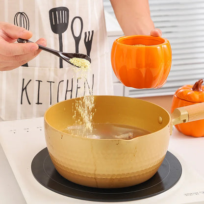 Person adding seasoning to a bowl of soup using a black spoon, with an orange container and pumpkin-shaped pot in the background. Pumpkin-shaped ceramic bowl with lid kitchen container Halloween and Thanksgiving fall serving dish