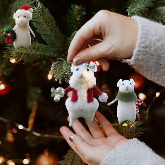 Hand holding a decorative mouse ornament with a Christmas tree in the background