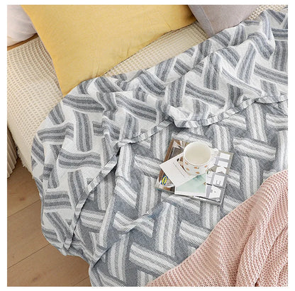 Gray and white chevron patterned blanket draped over a chair with a cup and magazine on it. Boho Lightweight microfiber summer blanket for bed or sofa, cooling breathable throw for home, dorm, or office naps with geometric jacquard pattern.