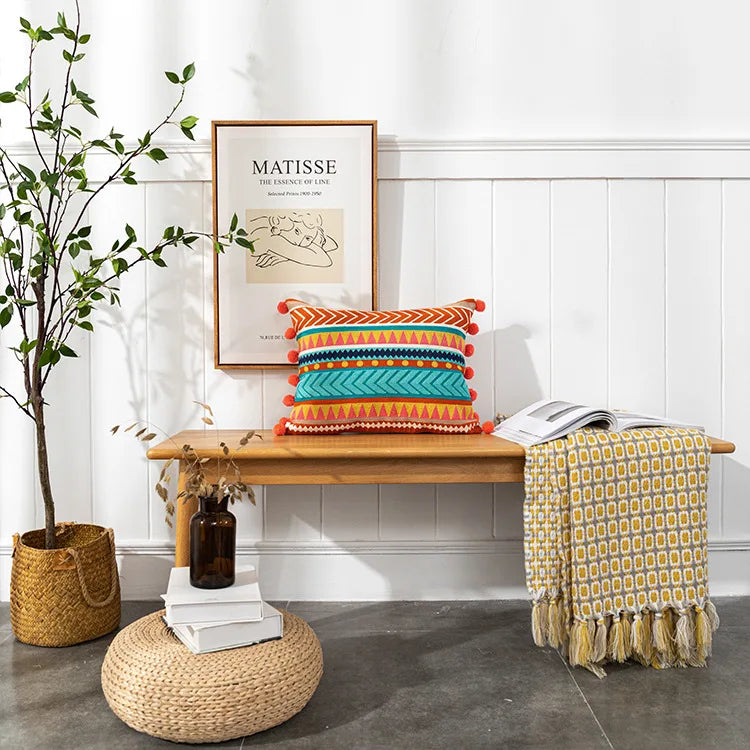 Colorful pillow on a wooden bench with a plant and books in the background. Bohemian embroidered throw pillow cover with geometric design, cotton-blend cushion for sofa, bed, or modern home decor.