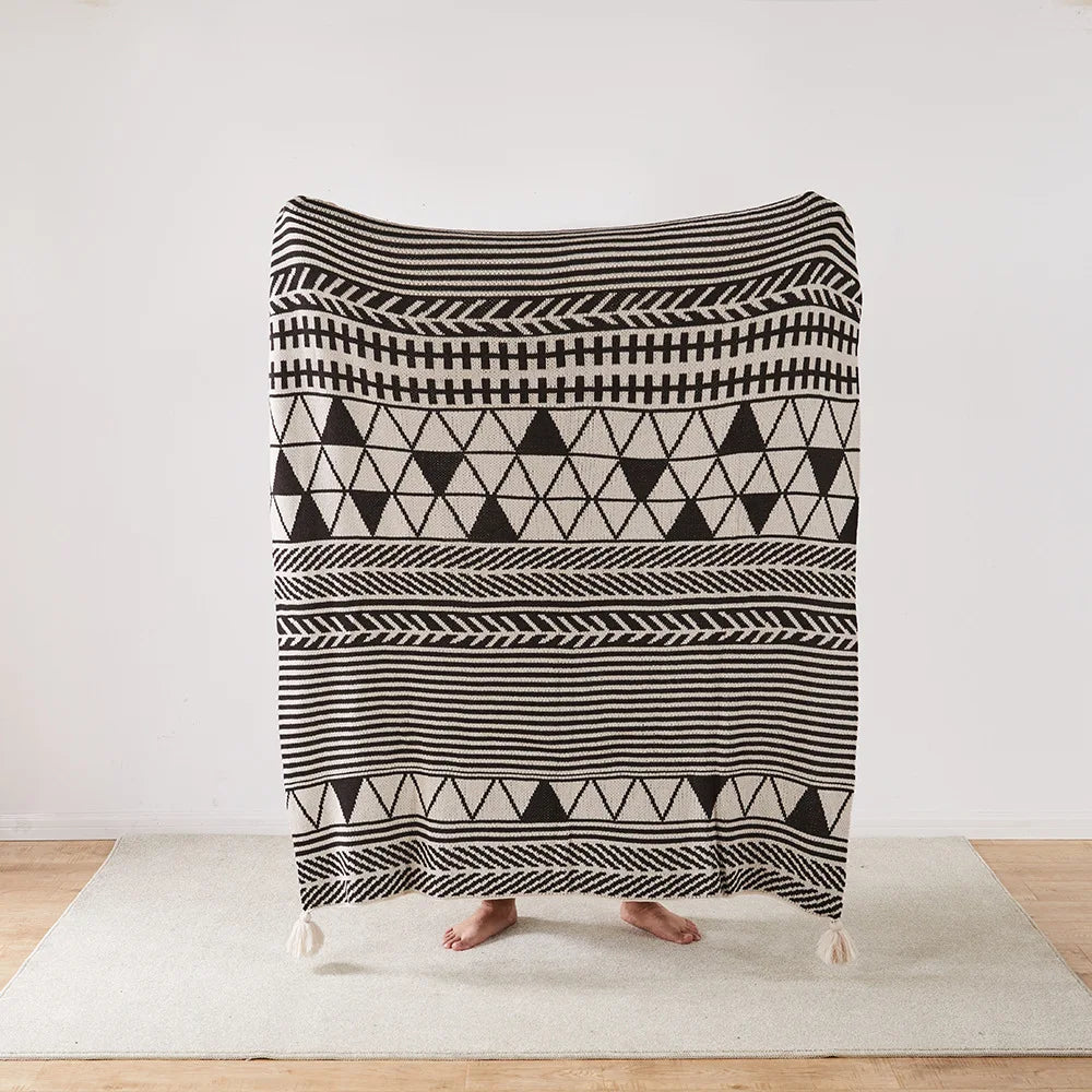 Person holding a black and white patterned Bohemian blanket on a wooden floor.