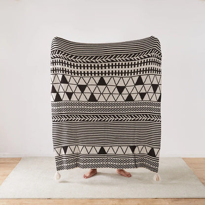 Person holding a black and white patterned Bohemian blanket on a wooden floor.