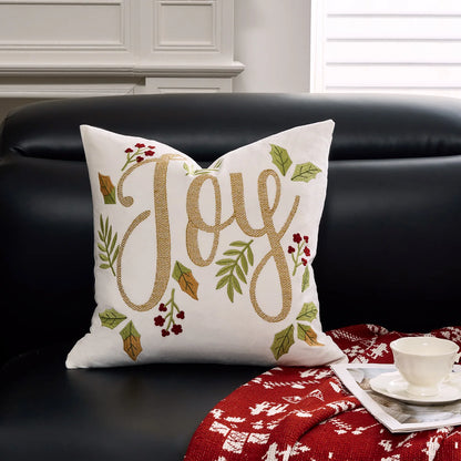 Decorative pillow with 'Joy' text on a black couch with a red blanket and white cup.