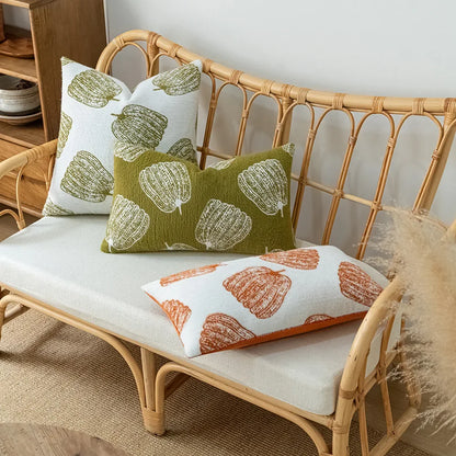 Wicker bench with patterned cushions on a neutral background. Cozy fall pumpkin pillow cover for living room or bedroom.