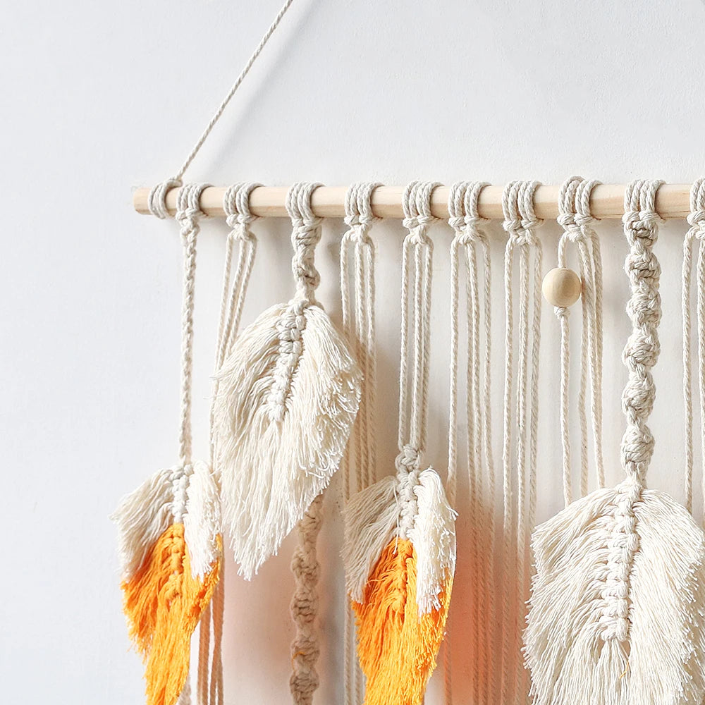Macrame wall hanging with white and orange tassels on a light background